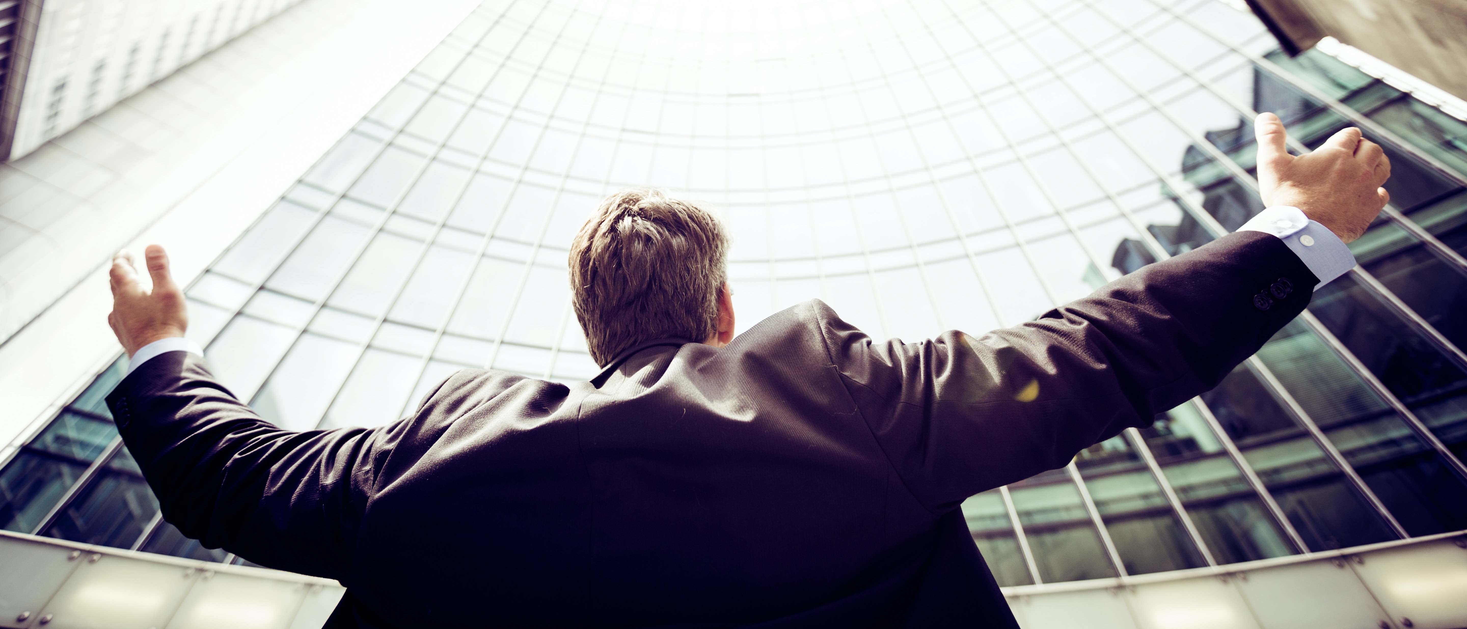 Man looking up the sky scrapper with open hands indicating the benefits